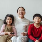 Parent and two children holding a remote together on a living room sofa