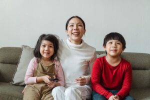 Parent and two children holding a remote together on a living room sofa