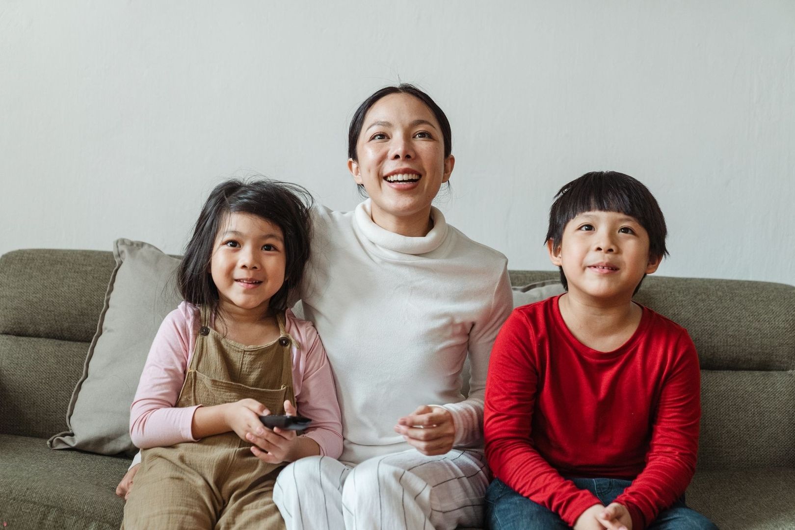Parent and two children holding a remote together on a living room sofa