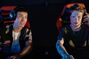 Two young people wearing headsets play games in illuminated gaming chairs