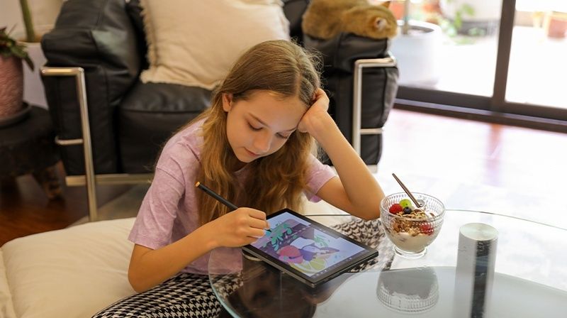 Child using a stylus on a tablet at a table beside a snack