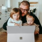 Parent and two children looking at a tablet together at a kitchen table